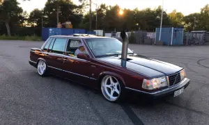 En mörkröd Volvo 760 D24 med en vertikal avgasrör som sticker upp från motorhuven. Bilen har vita fälgar och är parkerad på en asfalterad yta.