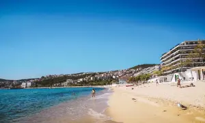Słoneczna plaża w Grecji, turkusowe morze, białe budynki na wzgórzu. Idealne miejsce na wakacje, gdzie grecja ceny są przystępne.