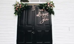 Eleganckie dekoracje na wesele: bukiety kwiatów i napis "It was always you" na czarnych drzwiach.
