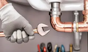 Hand mit Handschuh und Schraubenschlüssel arbeitet an Kupferrohren. Ein Projekt zur wasserleitung selbst verlegen wird hier gezeigt.