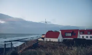 Vackra vita hus med röda tak vid havet, perfekt för en **weekendresa Danmark**. Gräs och staket i förgrunden.