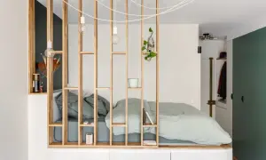 Un studio avec un coin nuit séparé par une étagère en bois. Le lit est fait de draps verts pâles.
