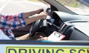 Osoba za kierownicą samochodu szkoleniowego pisze notatki. Zrozumienie, ile jest ważny egzamin teoretyczny prawo jazdy, to klucz do sukcesu.