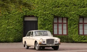 En klassisk Volvo 164 från 1973 parkerad framför en vackert klätterväxttäckt byggnad.