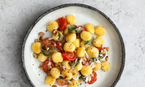 Pyszne gnocchi z sosem pomidorowym, listkami szałwii i orzechami laskowymi, posypane parmezanem.