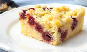 Ein Stück saftiger Kirschstreuselkuchen vom Blech auf einem weißen Teller, mit vielen Kirschen und knusprigen Streuseln.