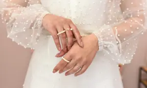 Dłonie panny młodej ozdobione pierścionkami z perłami, na tle sukni ślubnej z delikatnymi koralikami. Perły na ślubie dodają elegancji.