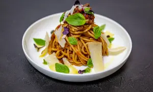 Pyszne spaghetti alla norma z sosem pomidorowym, bakłażanem, bazylią i parmezanem, podane na białym talerzu.