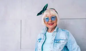 Modna starsza pani w okularach i jeansowej kurtce. Jej stylizacje, w tym spodnie z dziurami, są odważne i pełne życia.