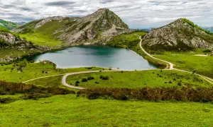 Un lago sereno rodeado de verdes colinas y picos rocosos, un paisaje idílico para ver Picos de Europa.