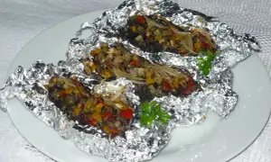 Kaszanka z grilla z cebulą i warzywami, zapieczona w folii aluminiowej, podana na białym talerzu.