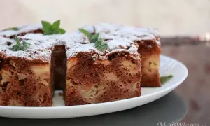 Wilgotne ciasto czekoladowe z jabłkami, posypane cukrem pudrem i udekorowane miętą.