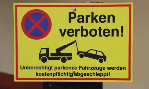 Gelbes Schild: Parken verboten! Ein Abschleppwagen holt ein schlecht geparktes Auto ab. Unberechtigt parkende Fahrzeuge werden kostenpflichtig abgeschleppt!