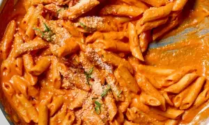 Penne alla vodka w kremowym, pomarańczowym sosie, posypane parmezanem i świeżą bazylią.