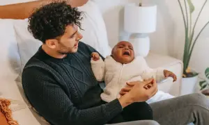Pappa tröstar sitt bebis som har ont i magen. Bebisen gråter intensivt medan pappan försöker lugna.