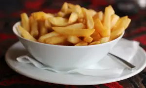 Chrupiące domowe frytki w białej misce na talerzyku z serwetką.