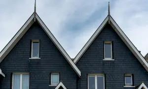 Dwa identyczne domy bliźniaki dwurodzinne projekt, pokryte ciemną łupkową dachówką, z białymi ramami okien i spiczastymi zakończeniami dachów.