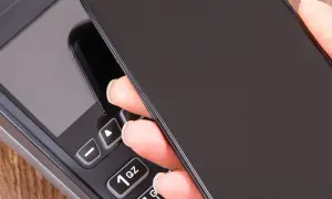 Zbliżenie na dłoń trzymającą telefon nad terminalem płatniczym. Szybki sposób, jak doladowac telefon Play.