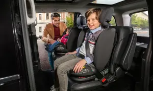 Padre sistema un bambino su un seggiolino auto, rispettando la normativa seggiolini auto. Un altro bambino è già seduto.