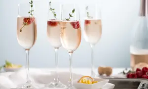 Quatre flûtes de soupe de champagne rosée, garnies de framboises et de thym, prêtes à être dégustées.