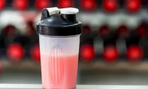Przezroczysty shaker z różowym napojem na tle czerwonych kółek.