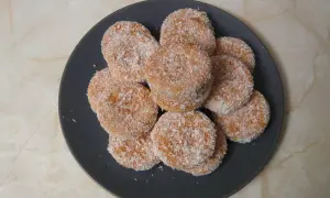 Montón de galletas de coco, doradas y cubiertas de coco rallado, apiladas en un plato oscuro.