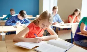 Uczniowie piszą w zeszytach, zastanawiając się, ile wynosi stypendium szkolne.