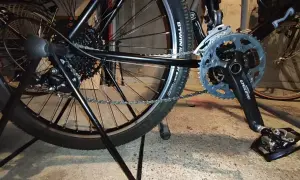 Widok tylnego koła i korby roweru. Pokazuje mechanizm przerzutek i łańcuch, który można naciągnąć, aby rower działał płynnie.