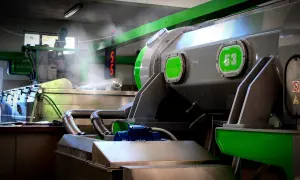 Macchinari industriali in una fabbrica, con tubi e vapore. Si intravede un cartello con "53", forse legato alla produzione di olio di sansa cos'è.