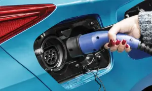 Dłoń z czerwonym lakierem na paznokciach wkłada niebieską wtyczkę do gniazda ładowania samochodu. To przyszłość motoryzacji – hybryda plug-in gotowa do jazdy.