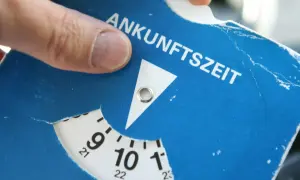 Ein Finger dreht die Scheibe einer Parkscheibe, um die Ankunftszeit einzustellen. So funktioniert eine Parkuhr: Zeit einstellen, auslegen, fertig.