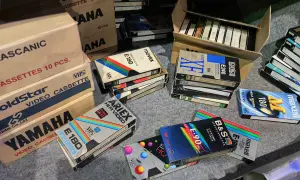 Kolekcja kaset VHS, w tym marki Movix, Konica, Maxell, Ariex, Yamaha. W tle pudełka z kasetami, przypominające o opłacie reprograficznej.