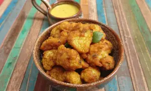 Beignets de choux-fleurs dorés et croustillants, servis dans un bol en terre cuite avec une sauce jaune crémeuse. Parfaits pour un apéritif savoureux.