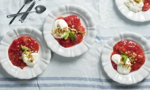 Tre vita skålar med rabarberkompott kardemumma, toppad med grädde och nötter. En härlig dessert.
