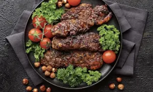 Saftiges Putenschnitzel braten, garniert mit Kirschtomaten, Petersilie und Haselnüssen auf schwarzem Teller.