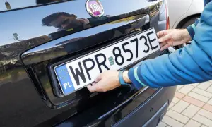 Ręce montują tablicę rejestracyjną WPR 8573E do czarnego Fiata. Zgubiona tablica rejestracyjna została odnaleziona.