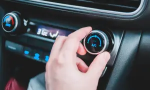 En hand vrider på reglaget för ac i bilen. Temperaturen sjunker snabbt.