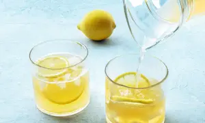 Erfrischendes Wasser mit Zitrone wird morgens in ein Glas mit Eis und Zitronenscheiben gegossen.