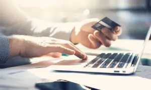 Dłoń trzyma kartę kredytową PKO, druga pisze na laptopie. Sprawdzam przejrzysta karta kredytowa PKO opłaty.