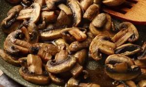 Gebratene Champignons in einer Pfanne, dampfend und glänzend, mit einem hölzernen Kochlöffel.