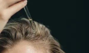 Tropfen eines Serums fallen auf die Kopfhaut, um das **Haarwachstum anzuregen**.