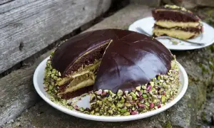 Torta al cioccolato con crema al pistacchio, ricoperta di glassa lucida e granella di pistacchio. Una fetta è già servita.