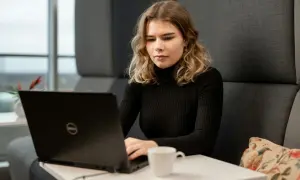 Młoda kobieta z wrodzonymi zdolnościami do pracy przy laptopie, skupiona na zadaniu. Obok filiżanka kawy.