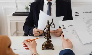 Adwokat w garniturze czyta dokumenty przy biurku, obok stoi Temida.