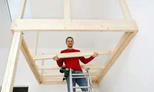 Man på en stege håller en träplanka, redo att bygga en stege till en loftsäng.