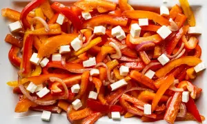 Bunter Paprika Salat mit roten Zwiebeln und weißen Würfeln, wahrscheinlich Feta-Käse.