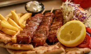 Pyszne souvlaki na patykach, podane z frytkami, pitą, sałatką i cytryną.