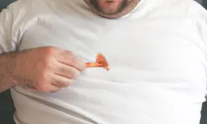 Ein Mann zeigt auf einen Ketchupfleck auf seinem weißen T-Shirt. Solche Fettflecken auf Kleidung sind ärgerlich.
