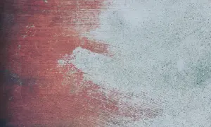 Texturen av ett betonggolv utomhus, delvis målat med röd färg. Penseldragen syns tydligt.