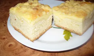 Puszyste ciasto drożdżowe z serem, z kruszonką na wierzchu, pokrojone na dwa kawałki na białym talerzu.